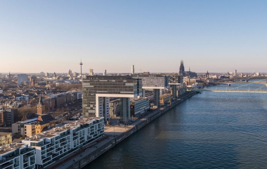 Stadtansicht mit Fluss und modernen Gebäuden, im Hintergrund der Kölner Dom.
