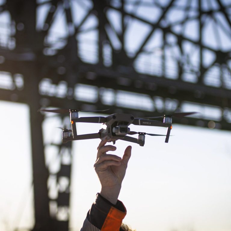 Eine Hand hält einen Drohnenquadrocopter vor einer Brücke.